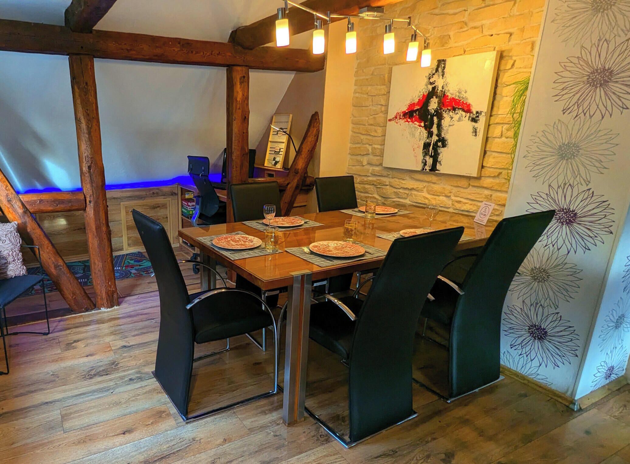 Un espace repas avec une table en bois, des chaises noires et un mur en pierre orné d’une fresque florale.