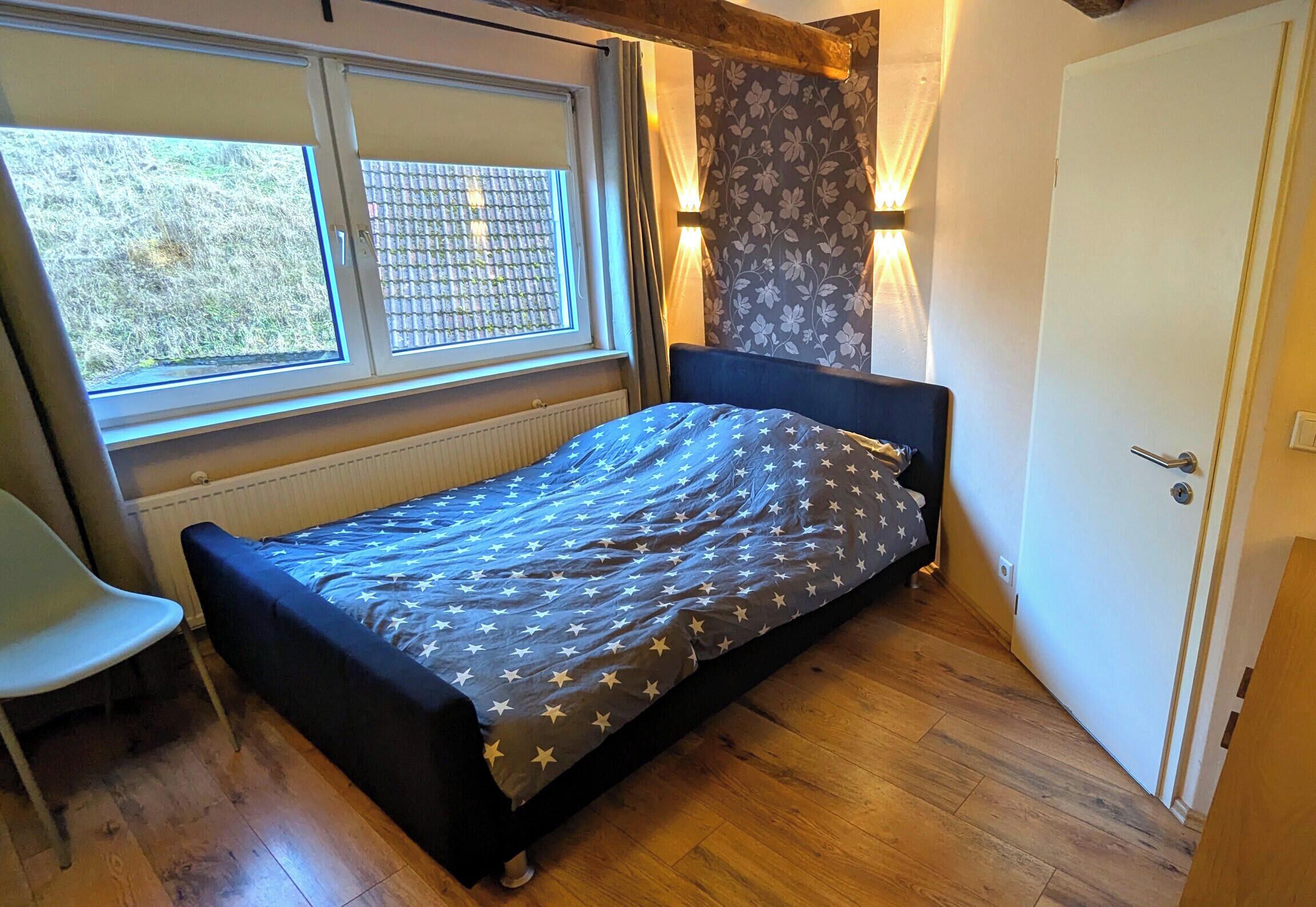 A small bedroom with a single bed, a chair, a window, and a door.