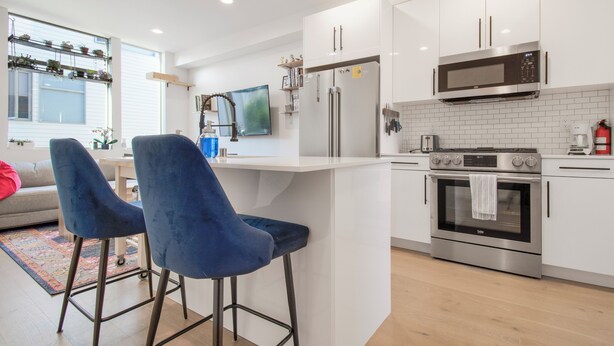 Una cocina moderna con gabinetes blancos, electrodomésticos de acero inoxidable y una zona de bar con sillas azules.