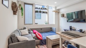 Una sala de estar moderna con un sofá gris, una mesita, un televisor y una ventana con persianas.