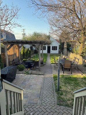 Zona de pati al jardí d'una casa amb una pèrgola, mobiliari d'exterior i un camí que hi mena.