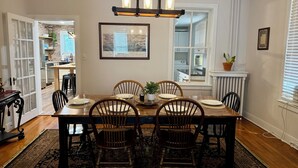A dining room with a wooden table, four chairs, a chandelier, a framed picture, and a view into the kitchen. - Beautiful Civil War home in Downtown Gettysburg! (Gettysburg)