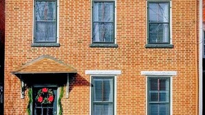 A two-story brick building with a front porch, three windows on the second floor, and a door with a wreath. - Beautiful Civil War home in Downtown Gettysburg! (Gettysburg)