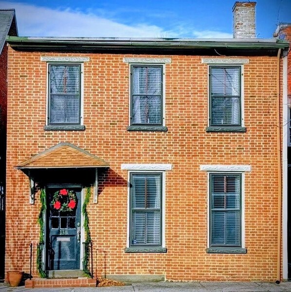 A two-story brick building with a front porch, three windows on the second floor, and a door with a wreath.