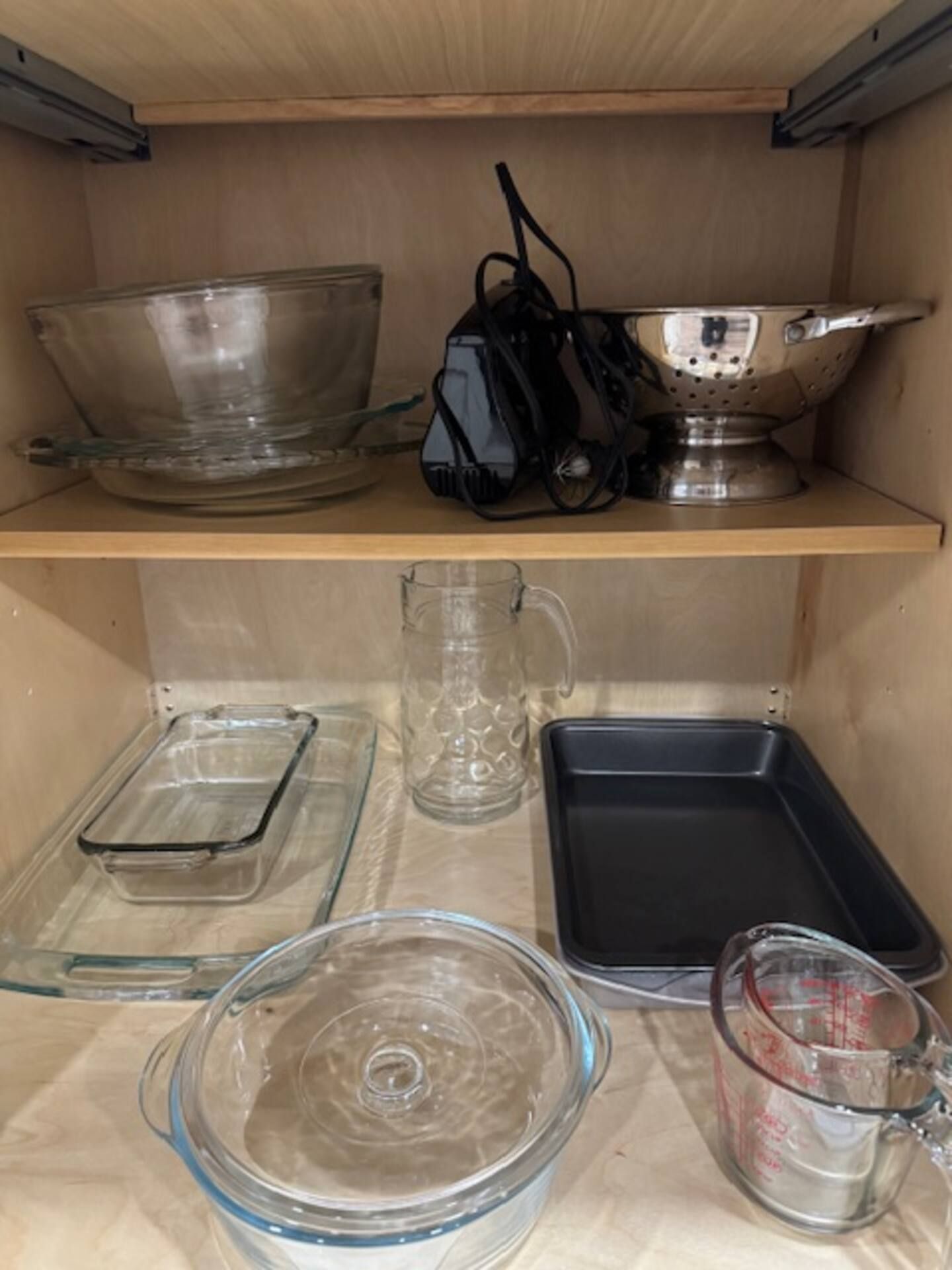 Una estantería de cocina con distintos utensilios de vidrio y cocina, incluyendo un vaso medidor, un bol de vidrio y un colador de metal.