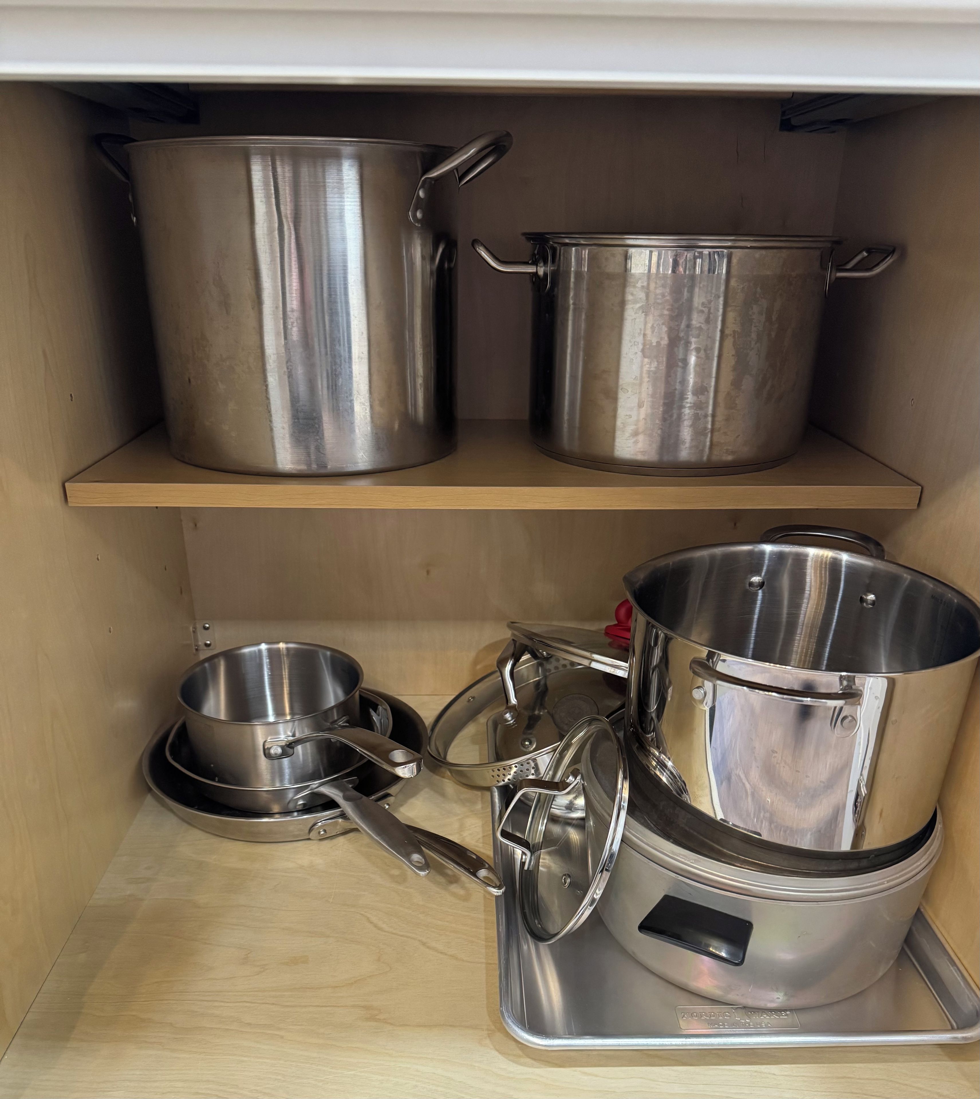 Una repisa de cocina con utensilios de acero inoxidable, incluyendo ollas, sartenes y una olla de cocción lenta.