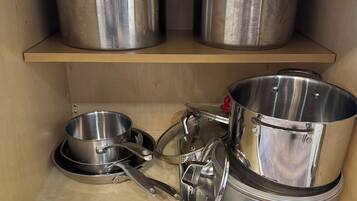 Una repisa de cocina con utensilios de acero inoxidable, incluyendo ollas, sartenes y una olla de cocción lenta.