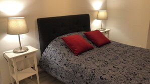 Quarto com cama, duas luminárias de cabeceira, mesa de cabeceira e uma gaveta.