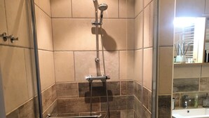 Chuveiro com porta de vidro, paredes azulejadas e piso estampado.