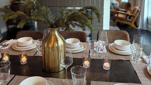 A dining area with a table set for four, featuring white plates, glasses, and a gold vase with greenery. - Luxury Walk-to-Stadium Stay with Backyard Retreat! (Tuscaloosa)