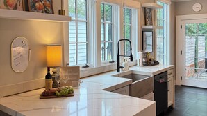 A modern kitchen with a marble countertop, built-in bar stools, and large windows. - Luxury Walk-to-Stadium Stay with Backyard Retreat! (Tuscaloosa)