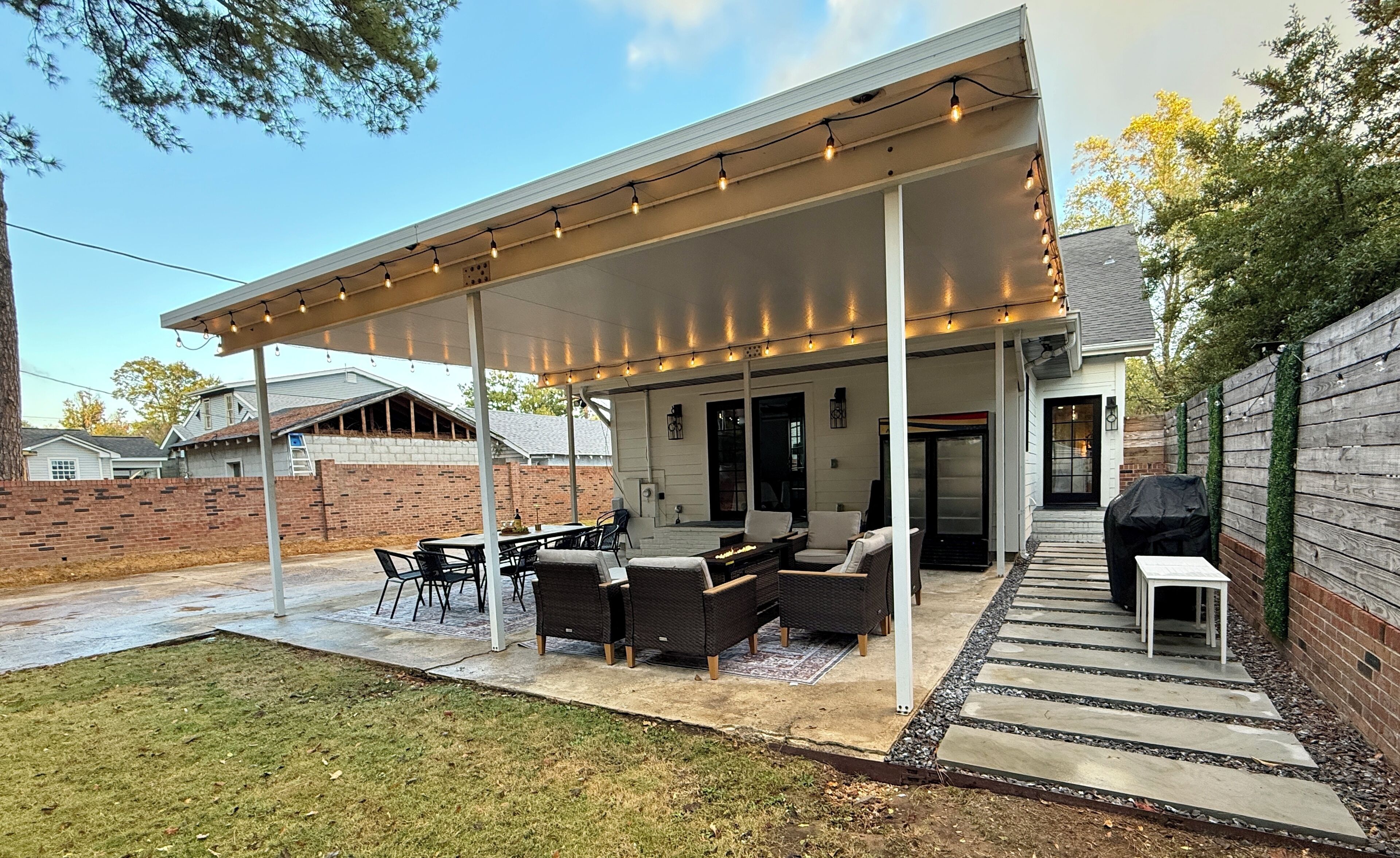 Ein überdachter Patio-Bereich mit Gartenmöbeln, einem Grill und Lichterketten.