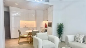 Uma sala de estar moderna com um sofá branco, uma mesa de centro de vidro e uma área de jantar com mesa e cadeiras brancas.
