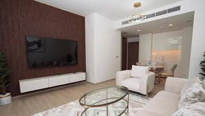 Uma sala de estar moderna com televisão de tela plana, sofás brancos, uma mesa de centro de vidro e uma parede de destaque em madeira.