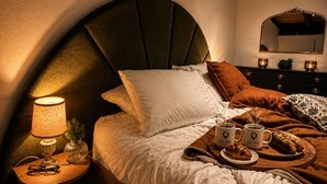 Ein Schlafzimmer mit einem gebogenen Kopfteil, einem Nachttisch mit Lampe, einem Spiegel und einer Ablage mit Croissants und Kaffeetassen.