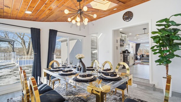 A dining area with a glass table, black and gold chairs, and a modern chandelier. - King Bed w/ Game Room near Massmutual w/ Riverview (Chicopee)