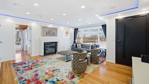 A modern living room with a fireplace, a colorful rug, and a seating area with ottomans. - King Bed w/ Game Room near Massmutual w/ Riverview (Chicopee)