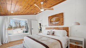 A bedroom with a wooden ceiling, a large bed with white bedding, a wooden headboard, a decorative mirror, and a nightstand with a bowl. - King Bed w/ Game Room near Massmutual w/ Riverview (Chicopee)