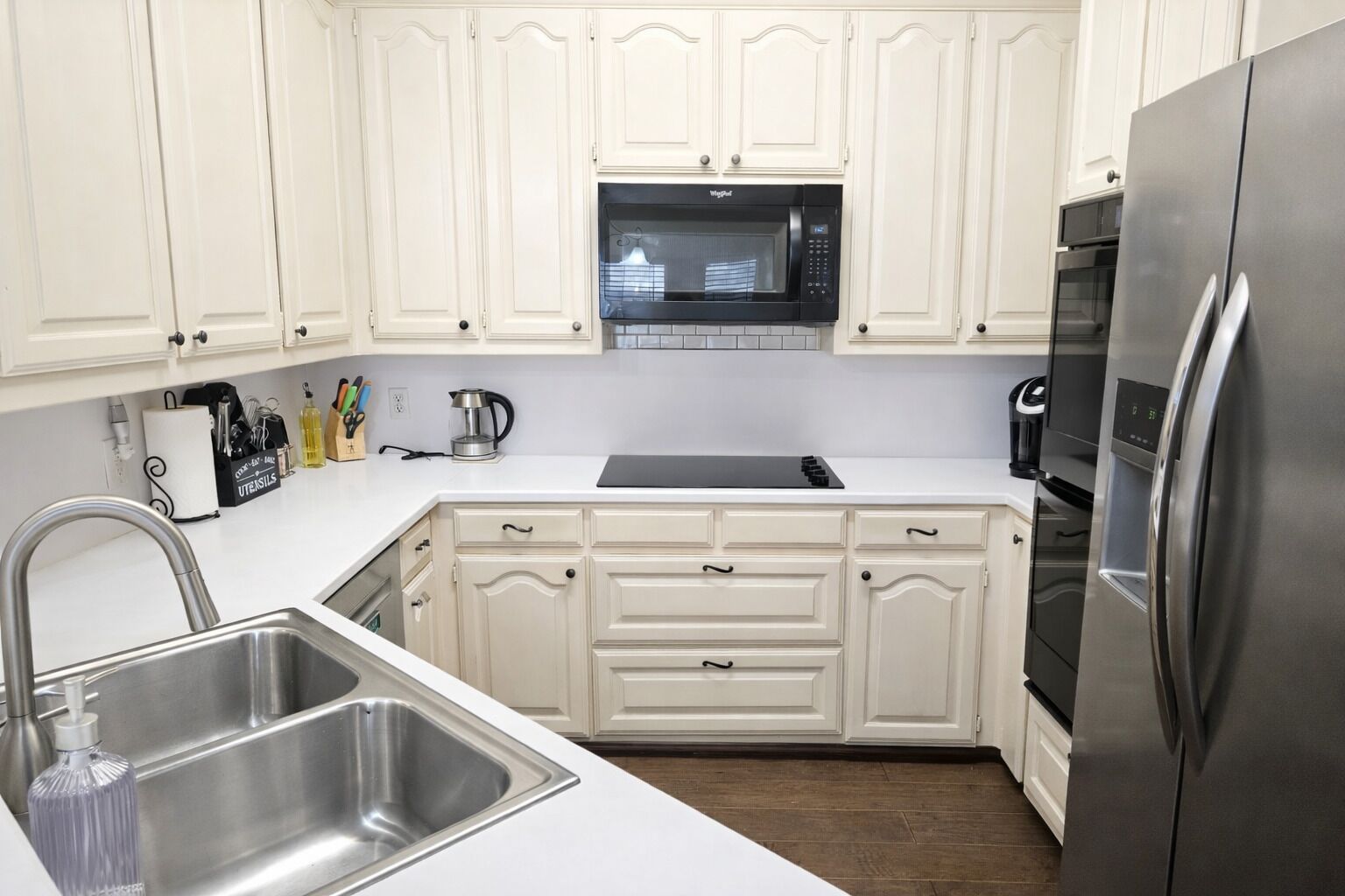 A kitchen with white cabinets, a stainless steel sink, a microwave, a coffee maker, and a refrigerator.