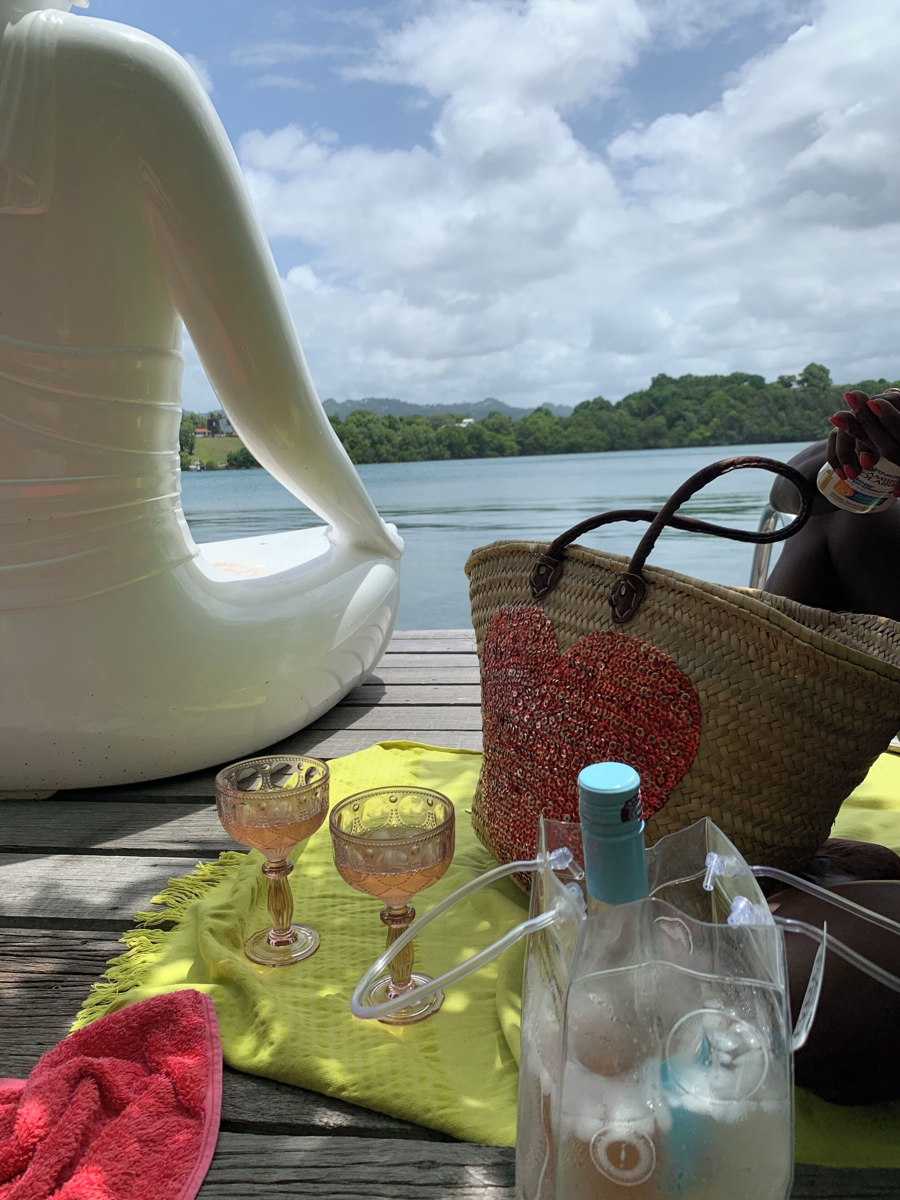 A wooden deck with a white chair, a woven basket, a bottle, and a glass pitcher.