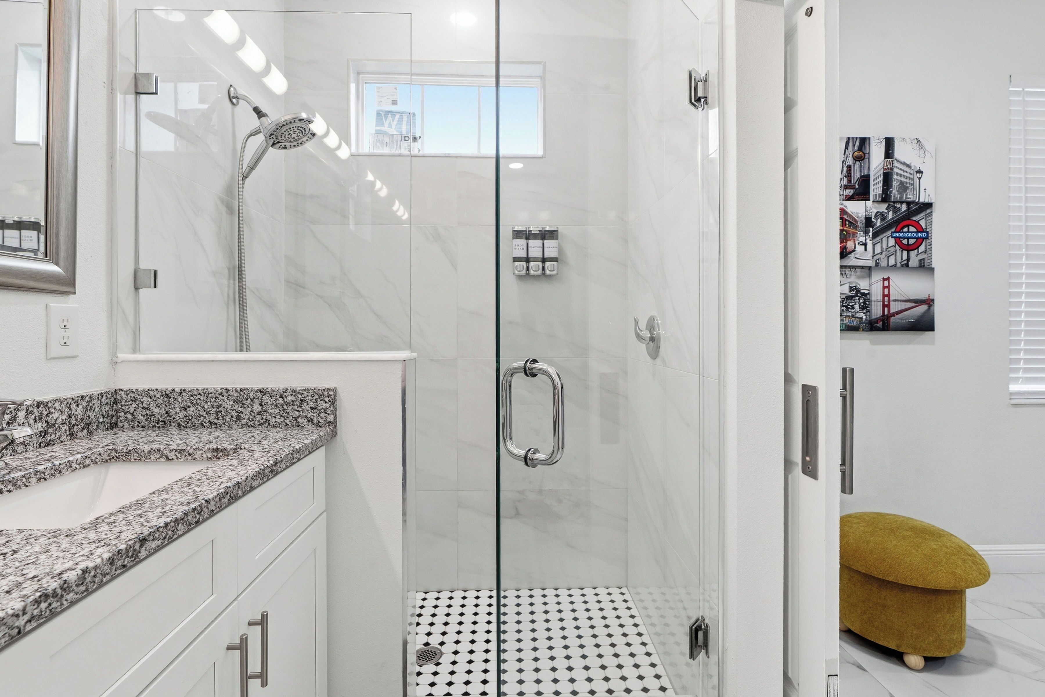A modern bathroom with a glass-enclosed shower, a granite countertop, and a small stool.