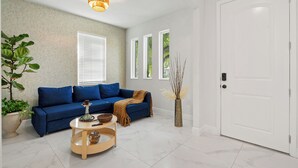 Een woonkamer met een blauwe bank, een ronde houten salontafel, een potplant en een witte deur.