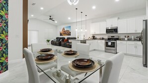 Een moderne keuken met witte kasten, roestvrijstalen apparatuur en een eethoek met een glazen tafel en witte stoelen.