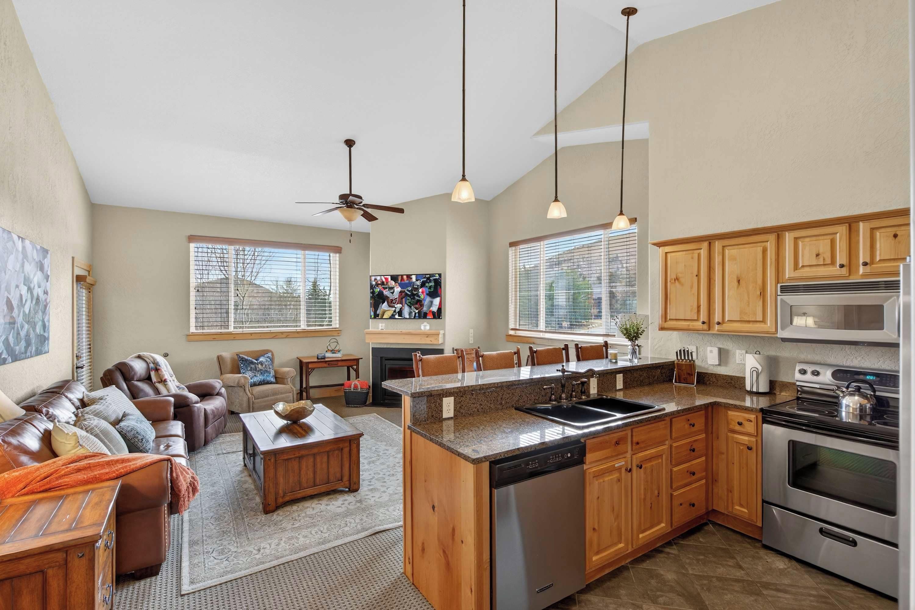 A spacious living area with a sofa set, a coffee table, and a fireplace. The kitchen features a granite countertop, stainless steel appliances, and wooden cabinets.