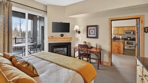 Quarto de hotel com cama, lareira, televisão, mesa de jantar e cozinha.