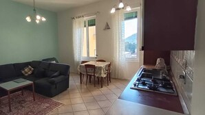 A living room with a sofa, a small table, and a dining area with chairs and a table. There is a kitchen with a stove and a window. - SANREMO IMPERATRICE CASINO' CITY CENTRE  threeroom flat for THE SANREMO FESTIVAL (Sanremo)