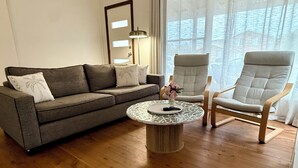 A living room with a grey sofa, two armchairs, a round coffee table, and a floor lamp. - Welcome to Saltwater Escape in Swansea. (Swansea)