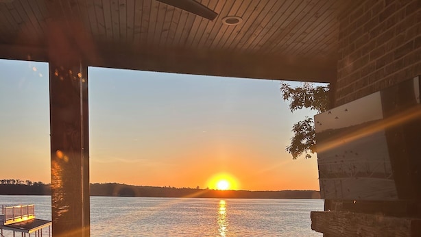 Puinen terassi, jolta avautuu näkymä auringonlaskuun veden yllä, katettu oleskelualue ja tiiliseinä.