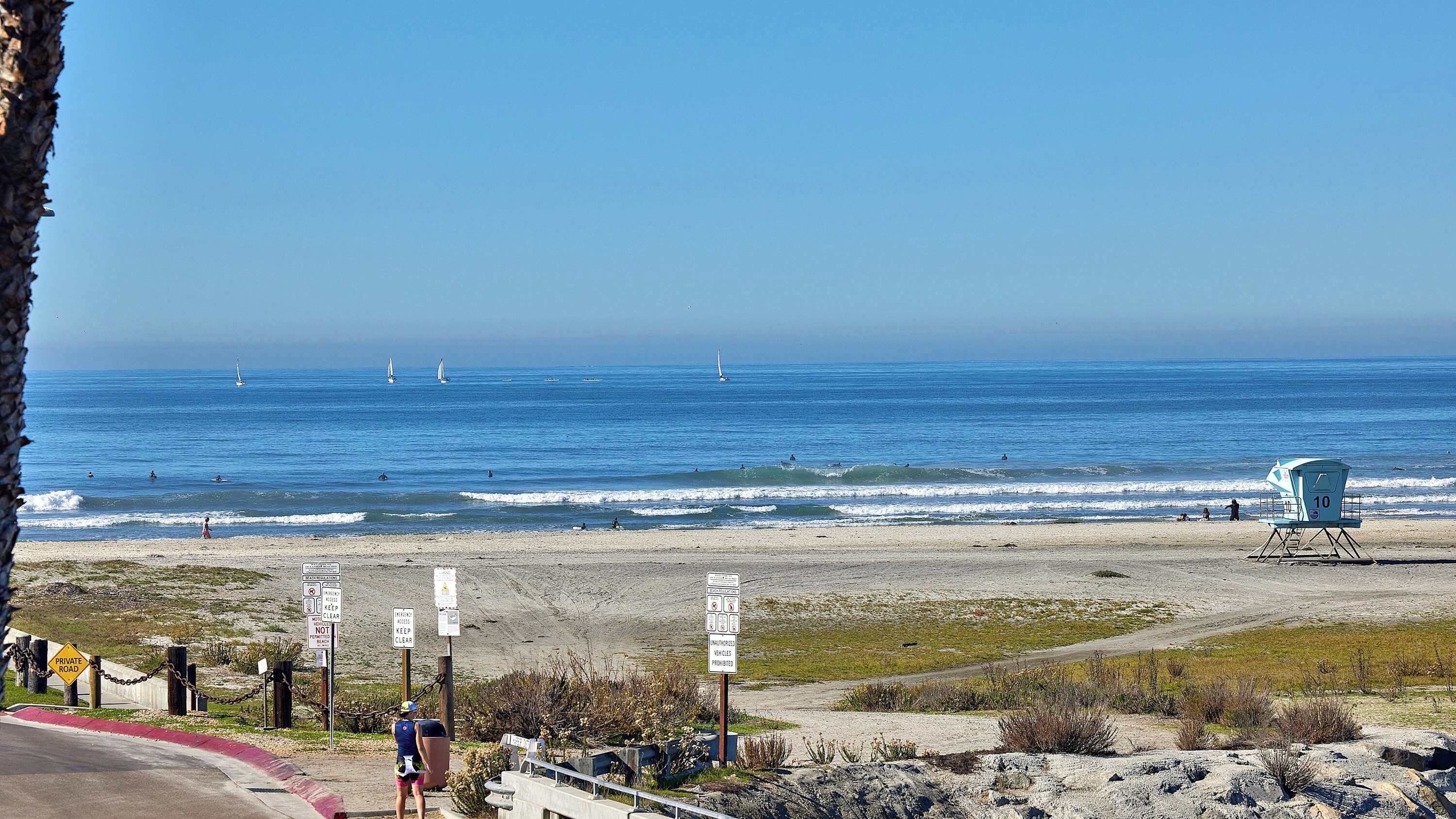 A beach with a lifeguard tower, clear skies, and a private road sign.