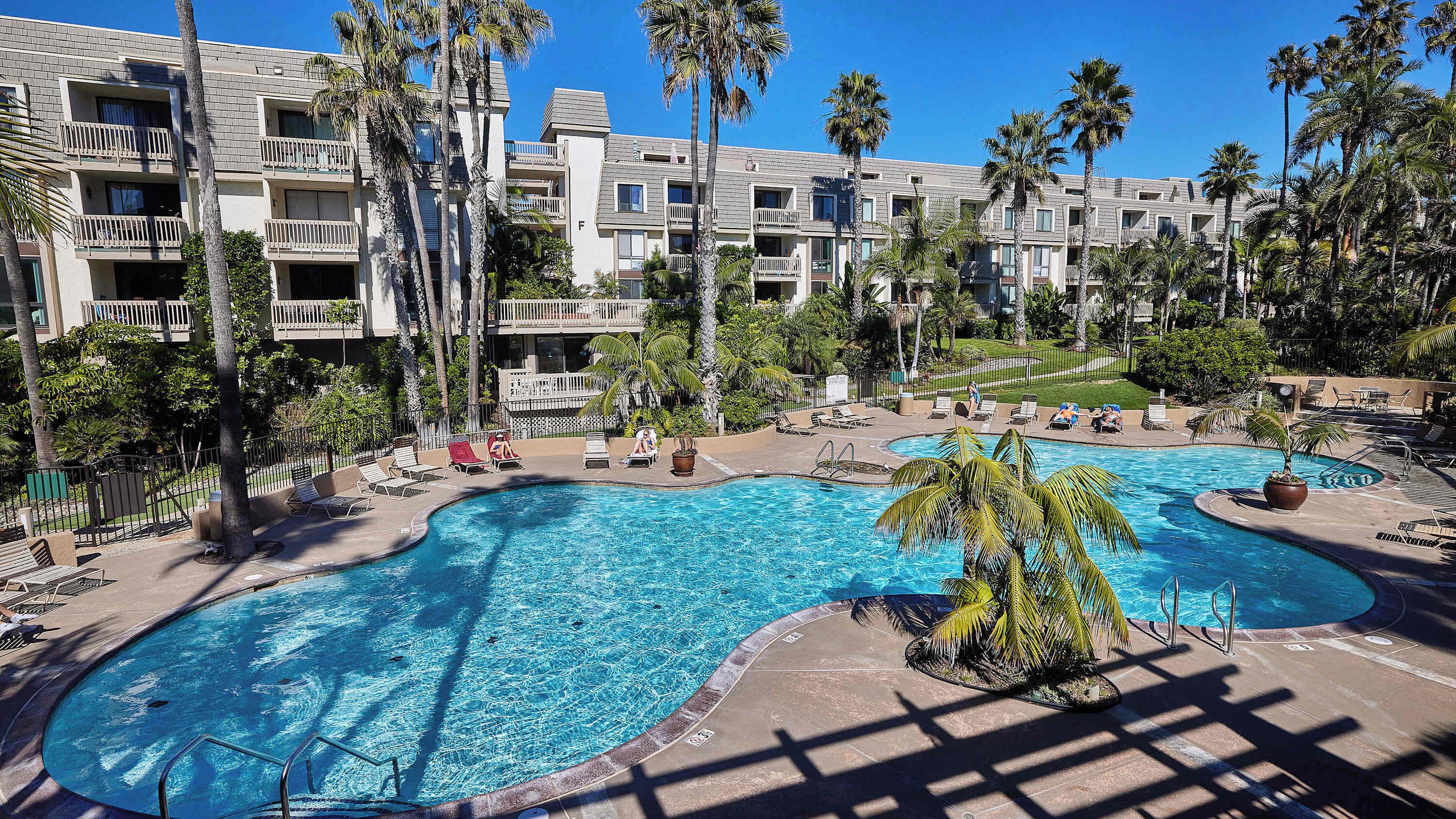 Un hotel con una amplia piscina rodeada de palmeras y sillones de descanso.
