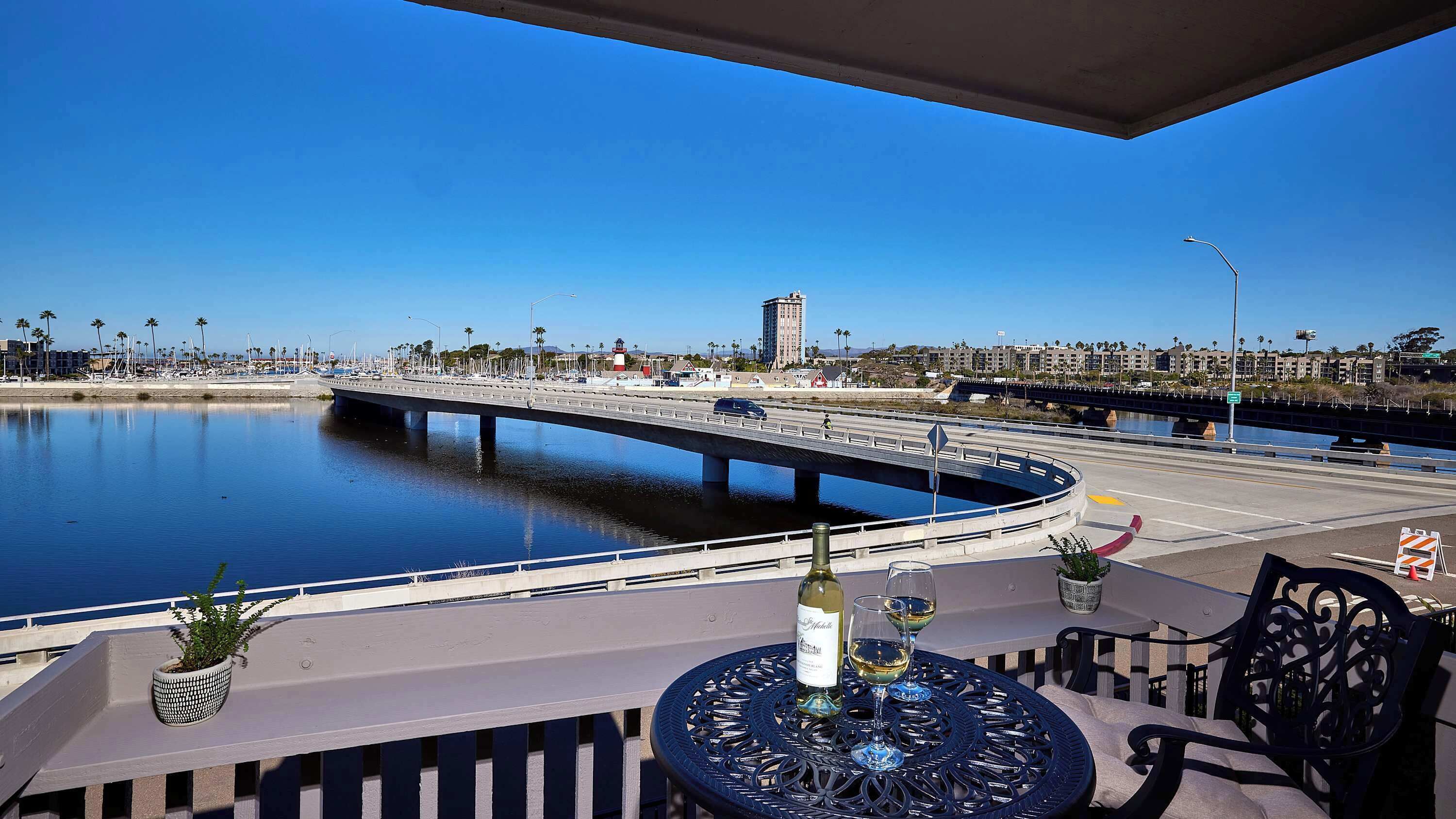 A waterfront patio with a view of a bridge, a marina, and a cityscape in the background.