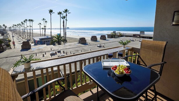 A balcony with a table set for two, overlooking a beach with palm trees and a pier. - North Coast Village D204 (Oceanside)