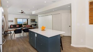 A modern kitchen with a central island, a dining area with a sofa and chairs, and a view of the ocean through large windows. - Oceanview Townhome Pvt.deck M-C (Oceanside)