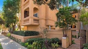 A building with a beige facade, a gated entrance, and a small garden with various plants. - Oceanview Townhome Pvt.deck M-C (Oceanside)