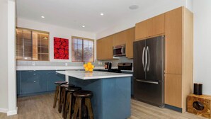 A modern kitchen with a central island, wooden cabinets, stainless steel appliances, and a blue accent wall. - Oceanview Townhome Pvt.deck M-C (Oceanside)