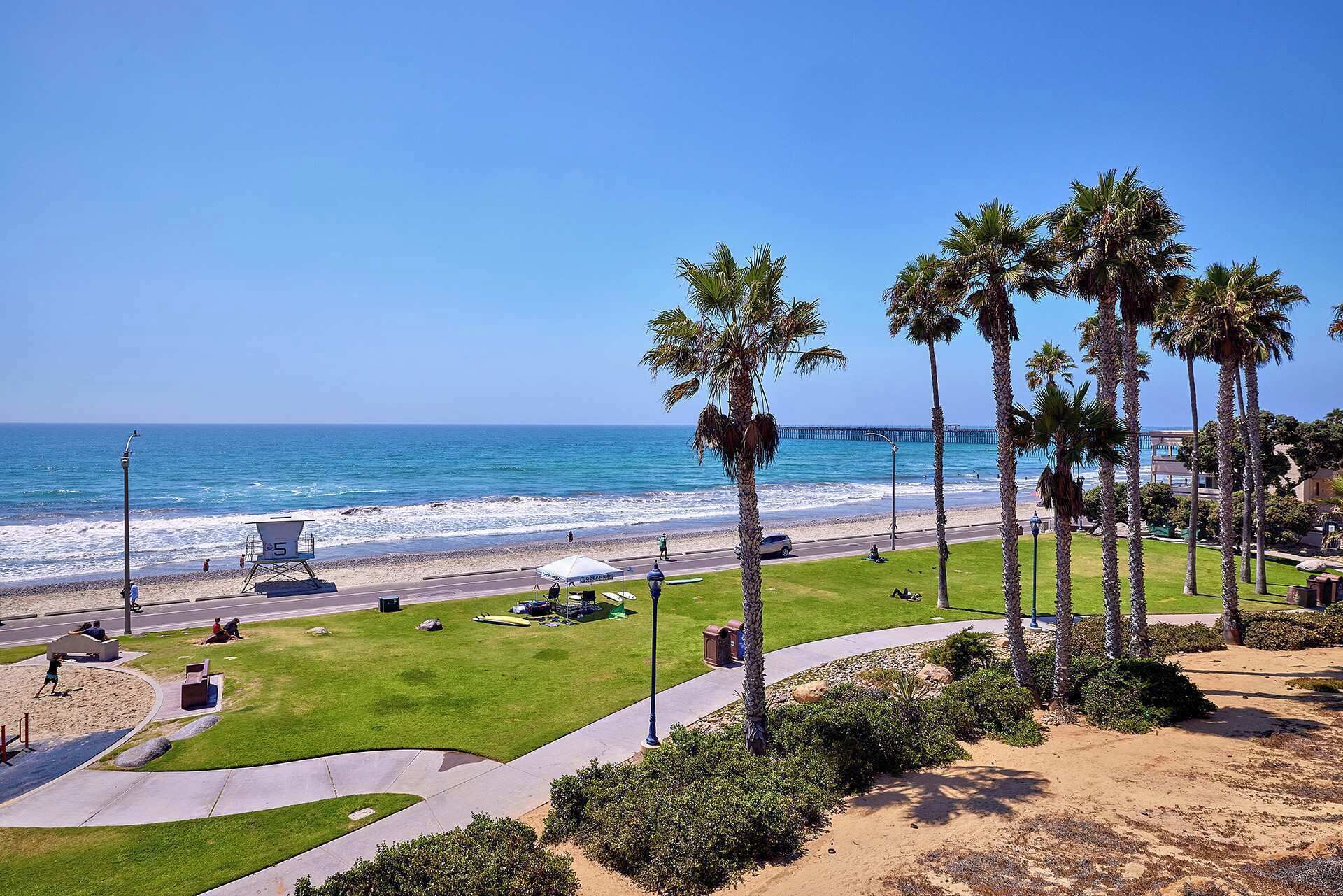 A beach view with palm trees, a lifeguard tower, and a pier in the background.