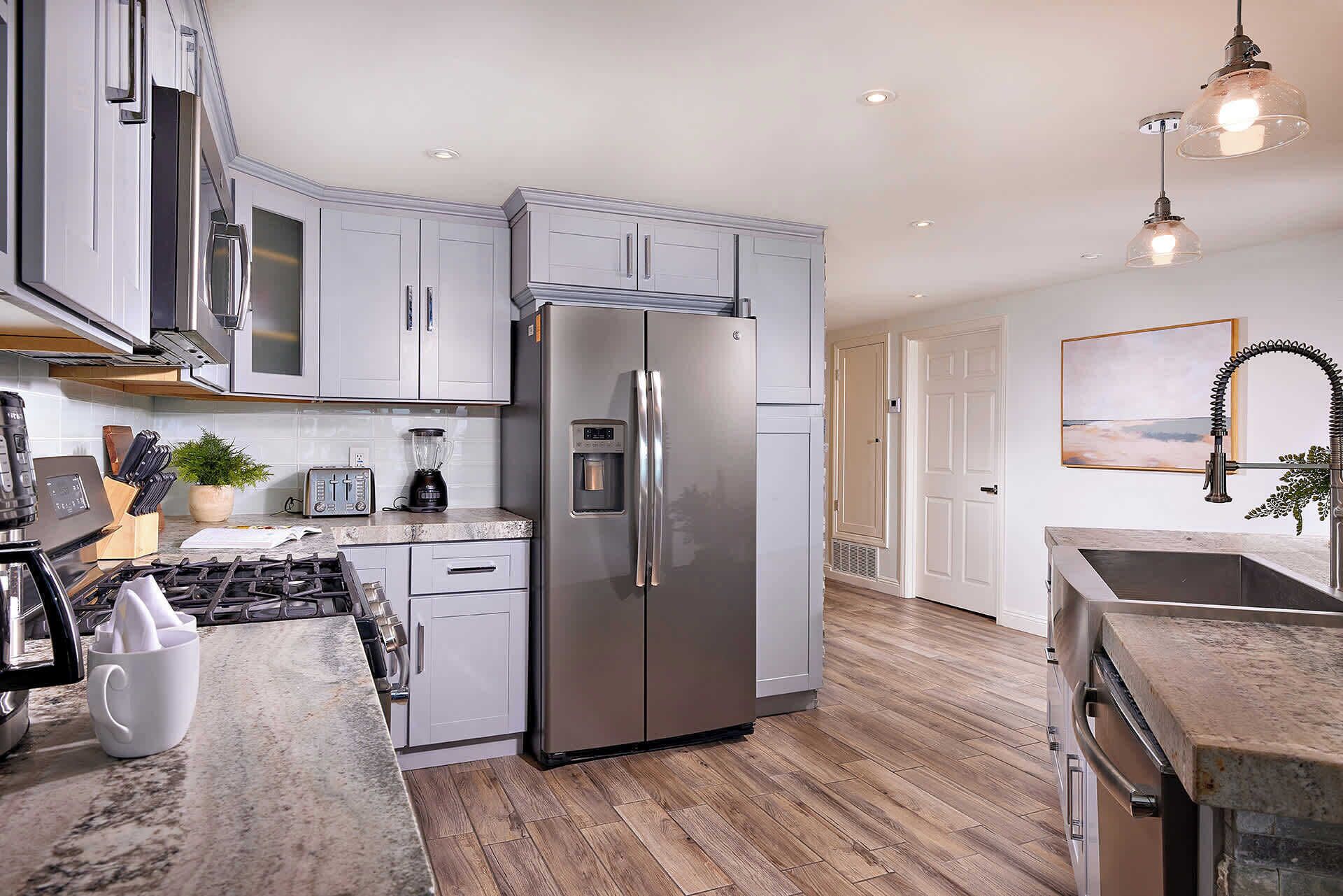 A modern kitchen with stainless steel appliances, white cabinetry, and a wooden floor.