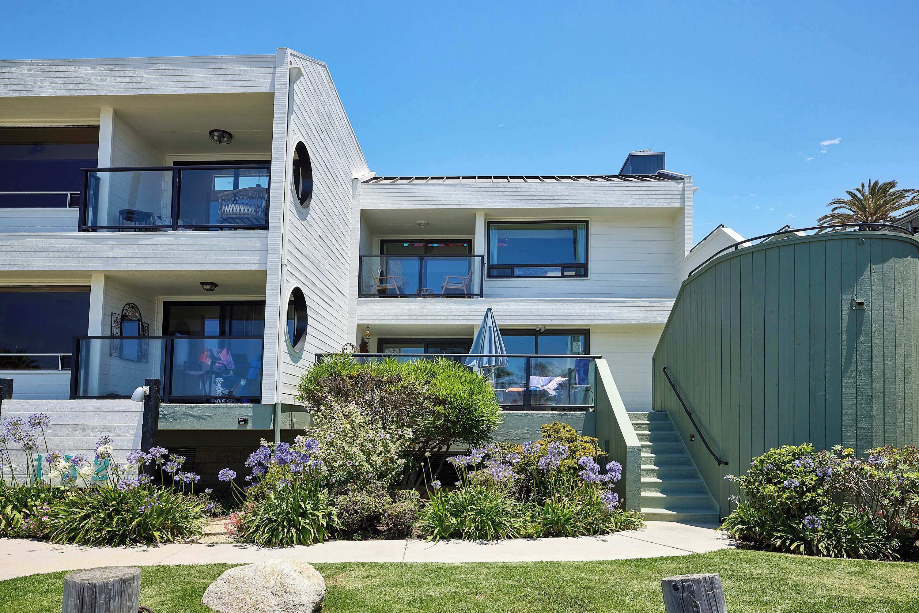 A multi-story residential building with balconies, a covered outdoor area, and a well-maintained garden.