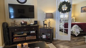 Un salon doté d’un téléviseur à écran plat, d’une table d’appoint en bois avec une lampe, d’une cheminée et d’un lit décoré d’une couronne de Noël.