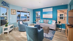 Una sala de estar con vista a la playa, un sofá, dos sillones, una mesita de centro y un mueble para la televisión.