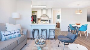 A modern living room with a sofa, a coffee table, and a dining area with chairs and a table. - Sunrise & Sunset by the Sea  812-1 (Oceanside)