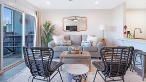 A living room with a sofa, two armchairs, a coffee table, a ceiling fan, a TV, and a large window. - Sunrise & Sunset by the Sea  812-1 (Oceanside)
