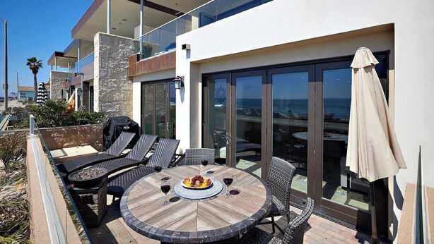 Een modern terras buiten met een ronde tafel, lounge fauteuils en een barbecue.