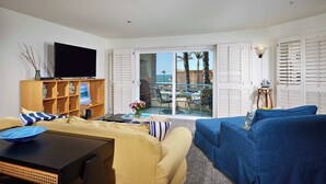 Ein modernes Wohnzimmer mit einer Couch, einem Couchtisch und einem Fernseher. Es gibt ein Holzschrank mit dekorativen Accessoires und Blick auf die Terrasse mit Tisch und Stühlen.
