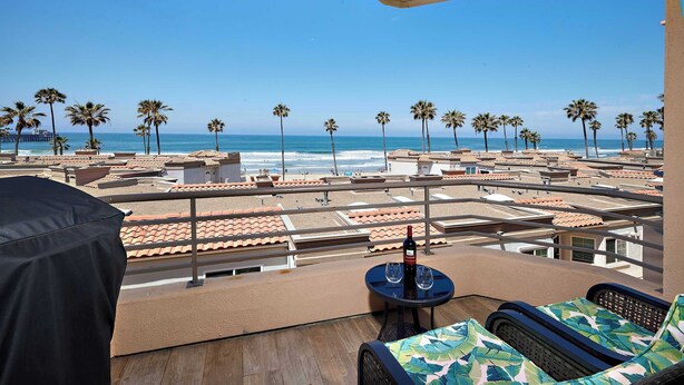 Une terrasse sur le toit offrant une vue sur la plage, les palmiers, ainsi qu’une table avec une bouteille et des verres.