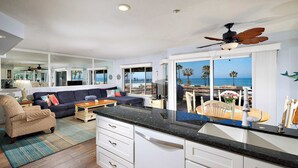 Une cuisine moderne dotée d’un grand îlot central, de meubles blancs et offrant une vue sur l’océan.